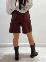 Bermuda color borgoña de gabardina elastizada, corte a la rodilla, con cinto fino con tachas y detalles de flecos en el ruedo.