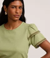 Blusa de manga corta color verde, con cuello redondo y detalles de terminación en efecto ganchillo en las mangas. Confeccionada en tejido de algodón con textura sutil.