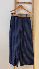 Pantalón de lino marrón con rayas verticales blancas, corte recto, cintura con elástico ancho y cinturón de rafia extraíble.