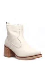 Bota corta de cuero color beige, con taco cuadrado de madera y plataforma baja. Presenta costuras decorativas laterales y tirador en la parte superior trasera.