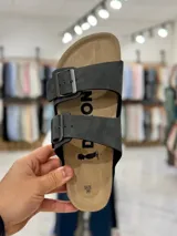 Sandalias de dos tiras negras con hebillas metálicas ajustables, plantilla anatómica y suela plana.