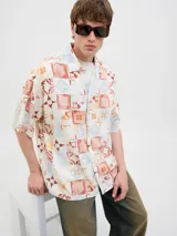Camisa de manga corta con cuello resort y fit amplio, confeccionada en tejido plano de lino y algodón. Presenta un estampado de mosaicos en tonos rojo, naranja, azul y blanco.