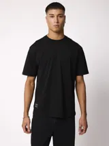 Remera negra de manga corta, cuello redondo y corte holgado, con pequeña etiqueta decorativa en el borde inferior.