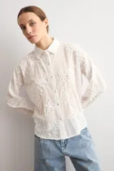 Camisa celeste con apliques florales bordados, cuello camisero, manga larga y cierre frontal de botones.