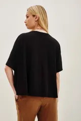 Remera negra de corte holgado con cuello redondo y mangas cortas. Presenta un aplique central en forma de corazón bordado con hilos y cuentas doradas, con un diseño detallado de aves en su interior.
