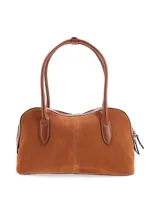Cartera tipo bowling de cuero gamuza color tostado, con doble asa de mano en cuero liso, cierre superior y logo metálico de la marca en el frente.