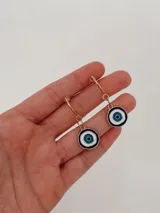 Aros tipo argolla con dije colgante en forma de ojo turco esmaltado en tonos azul, blanco y negro.