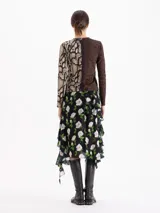 Pollera asimétrica de seda con estampado floral de rosas blancas sobre fondo negro. Presenta volados irregulares en forma de caracol que recorren el frente y la espalda, aportando volumen y movimiento.