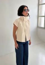 Top de algodón color crema, de manga corta y cuello alto estructurado. Cuenta con cierre frontal cruzado con botones metálicos a presión y costuras decorativas.