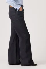 Jean de corte loose boot, tiro medio, color negro, con diseño de cinco bolsillos y cierre frontal con botón y cremallera.