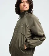Campera rompeviento color verde militar, con cierre frontal de cremallera, cuello alto, puños y cintura elásticos. Presenta recortes delanteros y un pequeño logo estampado en el pecho.