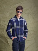 Camisa de manga larga en color azul noche con un patrón de cuadros finos en tonos rojos y verdes. Presenta cuello clásico, cierre frontal con botones y un bolsillo en el pecho con solapa.