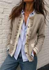 Chaqueta de punto color beige, con diseño de cuello redondo y cierre frontal de botones. Presenta detalles de volados desflecados en la solapa y bolsillos frontales, con puños acanalados a rayas.