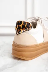 Zapatillas bajas de cuero color blanco y beige con suela marrón y detalle animal print en el talón.