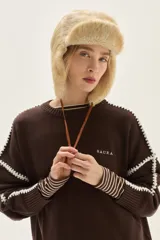 Sweater de cuello redondo color marrón, con detalles de bordado en contraste en color blanco a lo largo de las mangas y hombros. Presenta puños con diseño de rayas horizontales y el nombre de la marca bordado en el pecho.