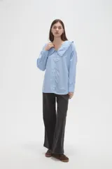 Camisa de algodón color celeste, con cuello grande tipo babero con volados, cierre frontal con botones y mangas largas con puños.