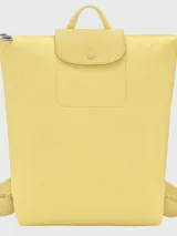 Mochila de diseño minimalista en color beige, con cierre superior de cremallera y solapa frontal con botón a presión. Presenta un asa superior y correas ajustables, con el logo de la marca grabado en la solapa.