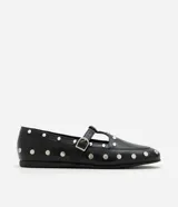 Zapato tipo salomé de color negro con acabado liso, puntera redondeada y suela plana. Presenta una tira central con hebilla metálica ajustable y está decorado con tachuelas metálicas plateadas distribuidas por toda la superficie.