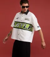 Camisa blanca oversized de tricolina con cuello negro contrastante, mangas cortas y estampado con la palabra "Hustle" en verde y negro.