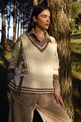 Sweater de punto estilo preppy en color crudo con detalles en marrón. Presenta cuello en V con ribete a rayas, tejido con textura de ochos y cordones laterales decorativos. Posee puños y ruedo acanalados con diseño a rayas.