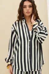 Camisa oversize de manga larga a rayas verticales en color negro y blanco, con cuello camisero y cierre frontal con botones.