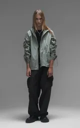 Campera rompevientos de diseño oversize, color verde, confeccionada en microfibra técnica ligera. Presenta capucha integrada, cierre frontal técnico y un sistema de frunces elásticos regulables a lo largo de las mangas que permiten ajustar el volumen de la prenda.