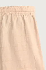 Shorts relaxed fit color beige con textura en relieve tipo jacquard, cintura elástica con cordón ajustable y detalle de bordado en contraste en el bajo.