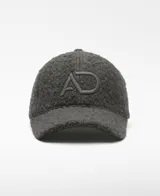 Gorra de seis paneles color gris oscuro, confeccionada en tejido de lana y poliéster con textura afelpada o borreguito. Presenta un logo bordado en el frente.