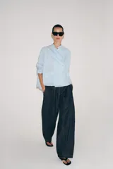 Camisa de corte oversize con estampado de rayas verticales, cuello redondo tipo mao y cierre frontal con botones. Presenta manga larga con puños anchos, un bolsillo de plastrón con solapa en el frente y bajo asimétrico.