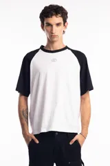 Remera de corte oversize con diseño tipo ranglan, que combina cuerpo blanco con mangas y cuello en color negro. Presenta un pequeño logo bordado en el centro del pecho.