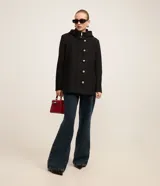 Saco corto negro de polivelour con capucha, cuello alto con cremallera, abotonado delantero cruzado, bolsillos delanteros y mangas largas.