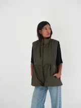 Chaleco verde seco con cuello alto, cierre frontal con cremallera y bolsillos laterales con cierre.