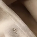 Canguro beige con capucha, cordones ajustables, bolsillo tipo canguro y logo estampado en el pecho.