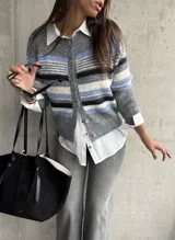 Saco tipo cardigan de punto con diseño de rayas horizontales en tonos gris, azul y blanco. Presenta cuello redondo, cierre frontal con botones y mangas largas.
