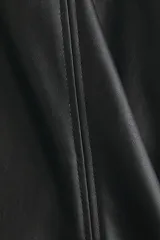 Pollera mini de corte evasé en color negro, confeccionada en material sintético con acabado tipo cuero. Presenta un diseño de cintura clásica y costuras verticales decorativas en el frente.