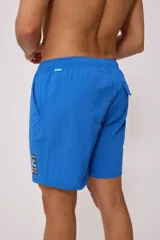 Short de baño tipo volley, color morado/rosado, con cordón ajustable en la cintura y un pequeño parche estampado en la pierna derecha.