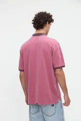 Remera polo de manga corta color rojo con efecto lavado, cuello y puños en contraste marrón. Cuenta con media cartera de botones, aberturas laterales en el dobladillo y un bordado pequeño de una estrella en el pecho.