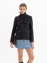 Chaqueta de paño gris con cuello mao y cuello desmontable con volados de gasa y puntilla. Presenta cierre frontal con botones metálicos, cuatro bolsillos delanteros con solapa y vivos en satén color chocolate que recorren el diseño.