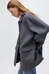 Abrigo de tejido afieltrado color gris oscuro, corte evasé, con cuello solapa y cierre frontal de botones oscuros. Presenta mangas raglán y dos bolsillos delanteros con solapa.