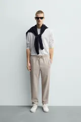 Pantalón jogger color beige de tejido transpirable y elástico con cintura elástica ajustable con cordón, bolsillos frontales y bajo con vuelta.