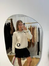 Buzo tejido a mano en color crudo, con diseño de herraduras bordadas en contraste negro y detalles de pespuntes en cuello, hombros y puños. Presenta un corte clásico de cuello redondo y mangas largas.