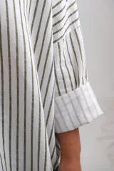 Blusa de corte oversize con estampado de rayas verticales en color verde sobre fondo blanco. Presenta cuello camisero con escote en V, mangas largas con puños anchos y un diseño holgado y fluido.