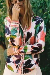 Camisa satinada de manga larga con cuello solapa y cierre frontal con botones, con un colorido estampado floral de estilo acuarela sobre fondo beige.