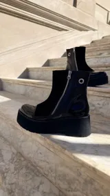 Botas cortas de cuero combinado en tonos tostado, marrón y detalles en charol negro. Cuentan con suela chunky, taco de 6 cm, cierre lateral y laterales de gamuza.