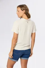 Camisa lisa de lino color beige, de manga corta, con cuello camisero, bolsillo ojal en el pecho y cierre frontal con botones.