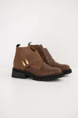 Bota corta de gamuza color chocolate, con suela track dentada y detalle de tira cruzada con apliques metálicos dorados.