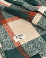 Sobrecamisa de paño con diseño a cuadros en tonos verde, blanco y detalles en naranja. Presenta cuello clásico, cierre frontal con botones, mangas largas con puños abotonados y dos bolsillos frontales con solapa en el pecho.