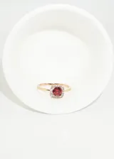 Anillo dorado con zirconia roja cuadrada rodeada de pequeñas zirconias blancas.