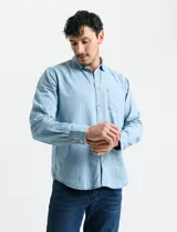 Camisa de denim de algodón con cuello clásico, cierre frontal con botones, bolsillo superior de parche y mangas largas con puños abotonados.