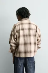 Camisa de algodón con cuello solapa, manga larga y dos bolsillos plastrón en el delantero. Presenta un patrón de cuadros en tonos beige y marrón oscuro.